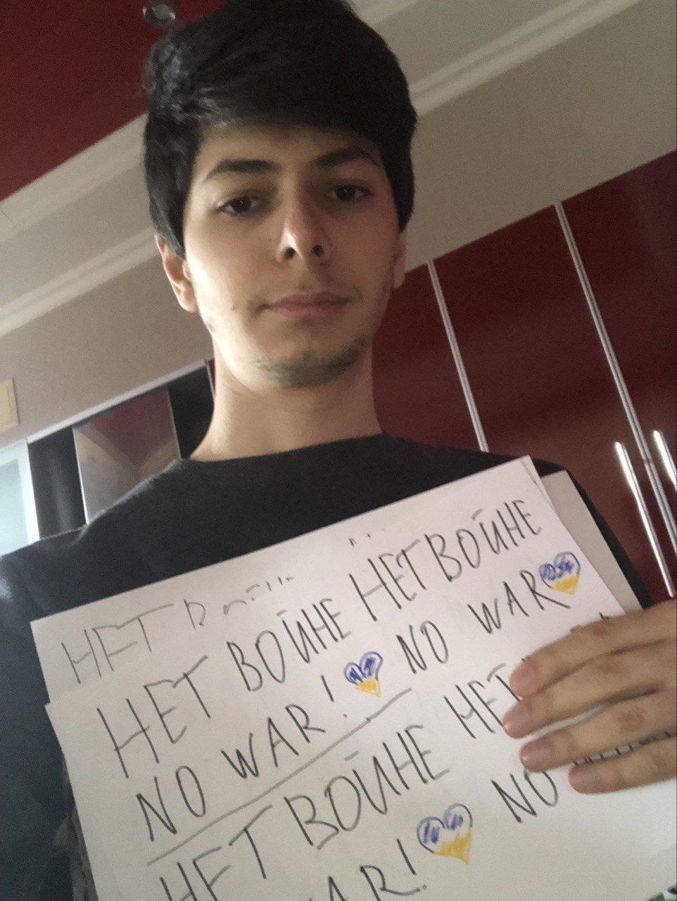 Тимур держит самодельные плакаты «Нет войне / No War» с украинскими флажными сердцами